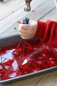 a child using a drill to paint red stained glass in a metal pan on the floor