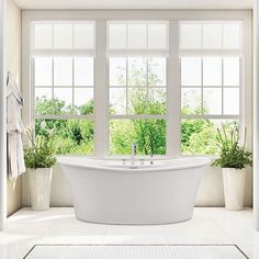 a white bath tub sitting in front of two windows next to potted planters