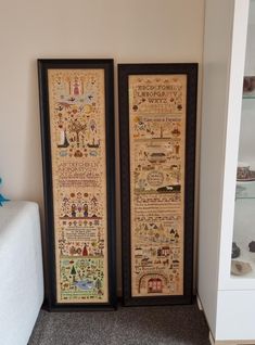 two framed cross stitch samples sitting next to each other on a shelf in a room