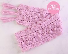 two crocheted pink scarfs with tasselled ends on a marble surface