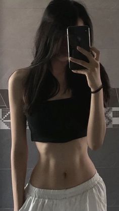 a woman taking a selfie in front of a mirror wearing white shorts and a black crop top