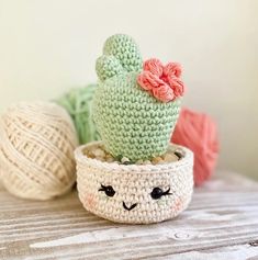 three crocheted cactus plants sitting on top of a table next to balls of yarn