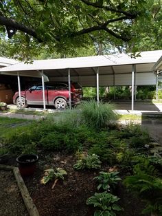 a red car is parked in front of a carport on the side of a house