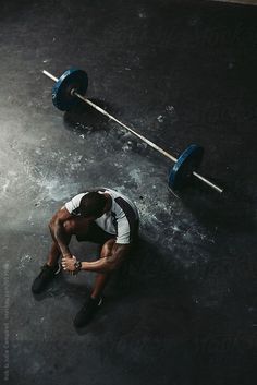 a man sitting on the ground with a barbell in his hand and looking down