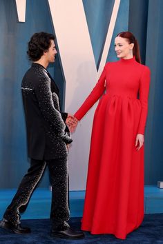 a woman in a red dress and a man in a black suit are holding hands