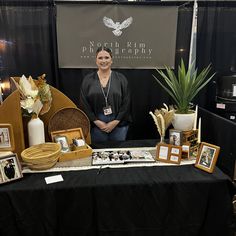 a woman standing behind a table with pictures and other items on it in front of a sign that says north rim photography