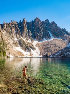 a person wading in the water near mountains