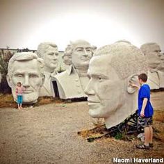 a man standing next to a giant statue of presidents