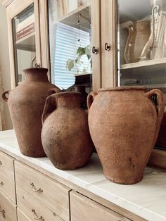 three brown vases sitting on top of a white counter next to a wooden dresser