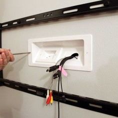 a person holding a pair of scissors in front of a wall mounted electrical outlet with wires attached to it