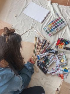 a woman sitting at a table with lots of art supplies and paintbrushes on it