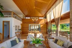 a living room filled with white couches and lots of wood furniture under a wooden ceiling