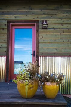 two large yellow vases sitting on top of a wooden table next to a red door