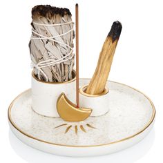 a white plate topped with two cups filled with sticks and an object in the middle