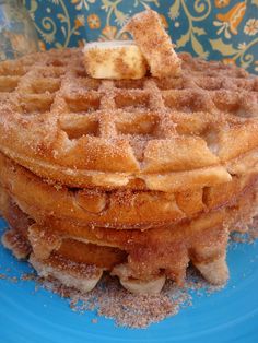 a stack of waffles sitting on top of a blue plate next to two jars of powdered sugar