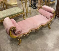 a pink couch sitting on top of a floor next to two tables and chairs with gold trimmings