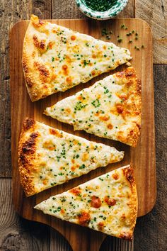 four slices of cheese pizza on a cutting board next to a bowl of green peas