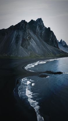 an aerial view of the black sand beach with mountains in the backgrouds