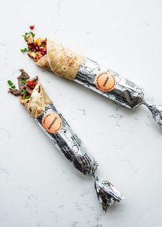 two burritos are sitting on a marble counter top, one has been wrapped in foil and the other is filled with vegetables