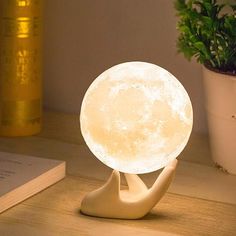 a white moon lamp sitting on top of a wooden table next to a potted plant