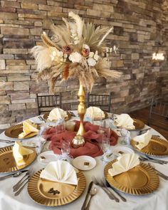 the table is set with gold and white plates, silverware, napkins, and flowers