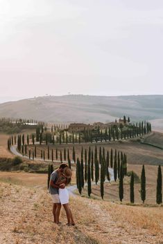 two people standing in the middle of a field with trees on either side of them