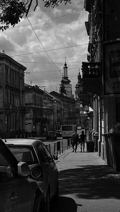 black and white photograph of people walking down the sidewalk in front of buildings on a cloudy day