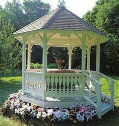 a white gazebo sitting in the middle of a lush green park filled with flowers