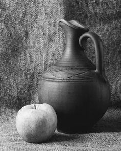 black and white photograph of an apple next to a vase on a gray cloth background