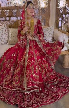 a woman in a red and gold wedding dress sitting on a bed with her hands clasped to her chest