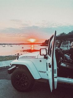 a man sitting in the driver seat of a white jeep with the sun setting behind him