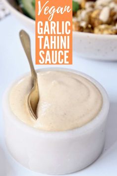 there is a small bowl of food with a spoon in it and a sign that says vegan garlic tahini sauce