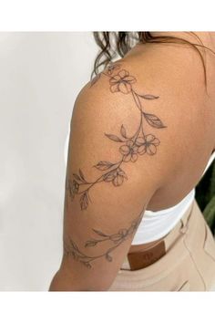 the back of a woman's shoulder with flowers and leaves tattooed on her arm