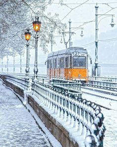 an orange train traveling down tracks next to snow covered street lamps and lampposts