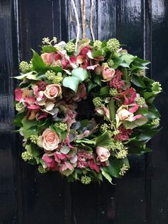 a wreath hanging on the front door with pink flowers and green leaves in it's center