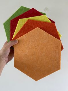 a hand is holding up several different colored felt hexagons that are stacked on top of each other