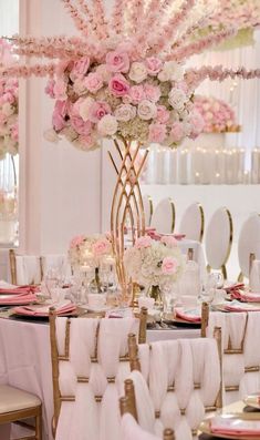 an elegant table setting with pink and white flowers on the centerpieces, gold chairs and candles