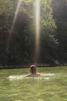 a woman is swimming in the water with trees in the backgrouds and sunlight shining down on her