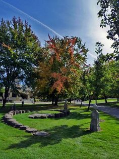 a grassy area with rocks and trees in the background on a sunny day at an urban park