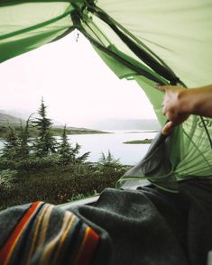 a person is camping in a tent with the view of water and trees behind them