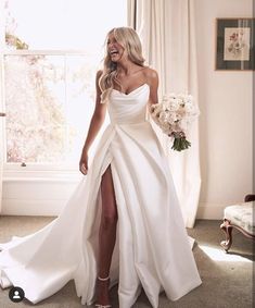 a woman in a white wedding dress standing next to a window with her legs crossed