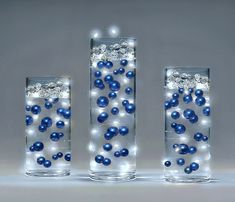 three glass vases with blue balls in them and lights on the bottom one is filled with water