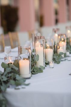 candles are lined up on a table with greenery