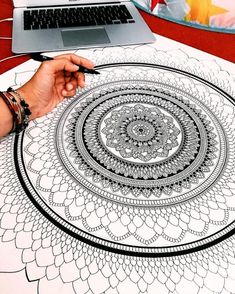 a person is using a pen to draw a circular design on a table with a laptop