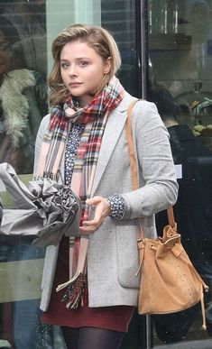 a woman is walking down the street with her hand in her pocket and wearing a scarf around her neck