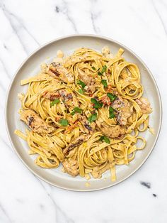 a white plate topped with pasta covered in sauce and meatballs on top of a marble table