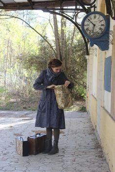 a woman standing in front of a building with luggage and a clock on the wall