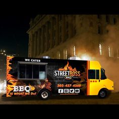 a black and yellow food truck parked in front of a tall building with flames coming out of it