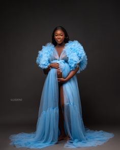 a pregnant woman in a blue gown with feathers on her head and arms, standing against a dark background