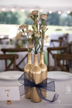 three gold vases with flowers in them on a table at a wedding or party